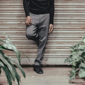 Stylish man posing casually against a roller shutter surrounded by plants.